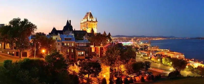 anoramic view of Old Quebec City at dusk, showcasing the illuminated Château Frontenac and historic buildings overlooking the St. Lawrence River