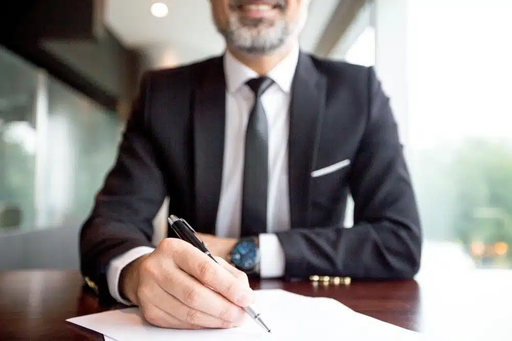 Professional tax lawyer in a suit signing documents at a desk, representing assistance with CRA wage garnishment services.