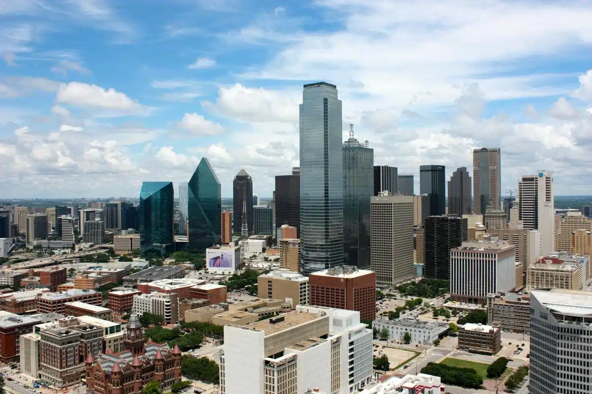 Aerial view of the Dallas, Texas skyline with modern skyscrapers and historic buildings under a partly cloudy sky.