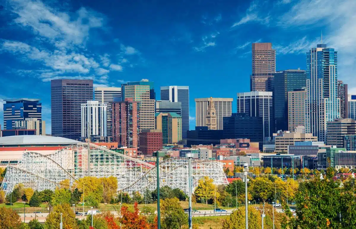 Vibrant view of the Denver, Colorado skyline with modern skyscrapers, amusement park, and fall foliage under a blue sky