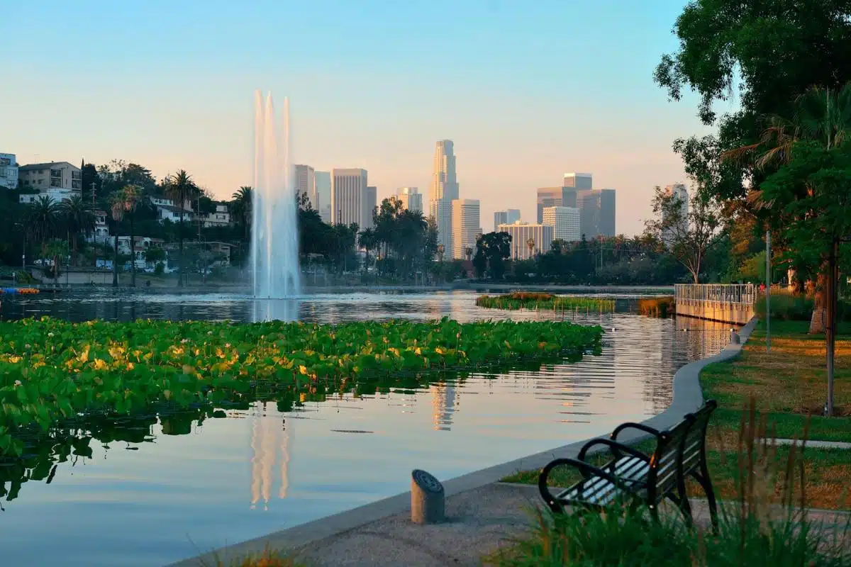 "Scenic view of Echo Park Lake in Los Angeles, California, with a water fountain, greenery, and downtown skyline at sunset.