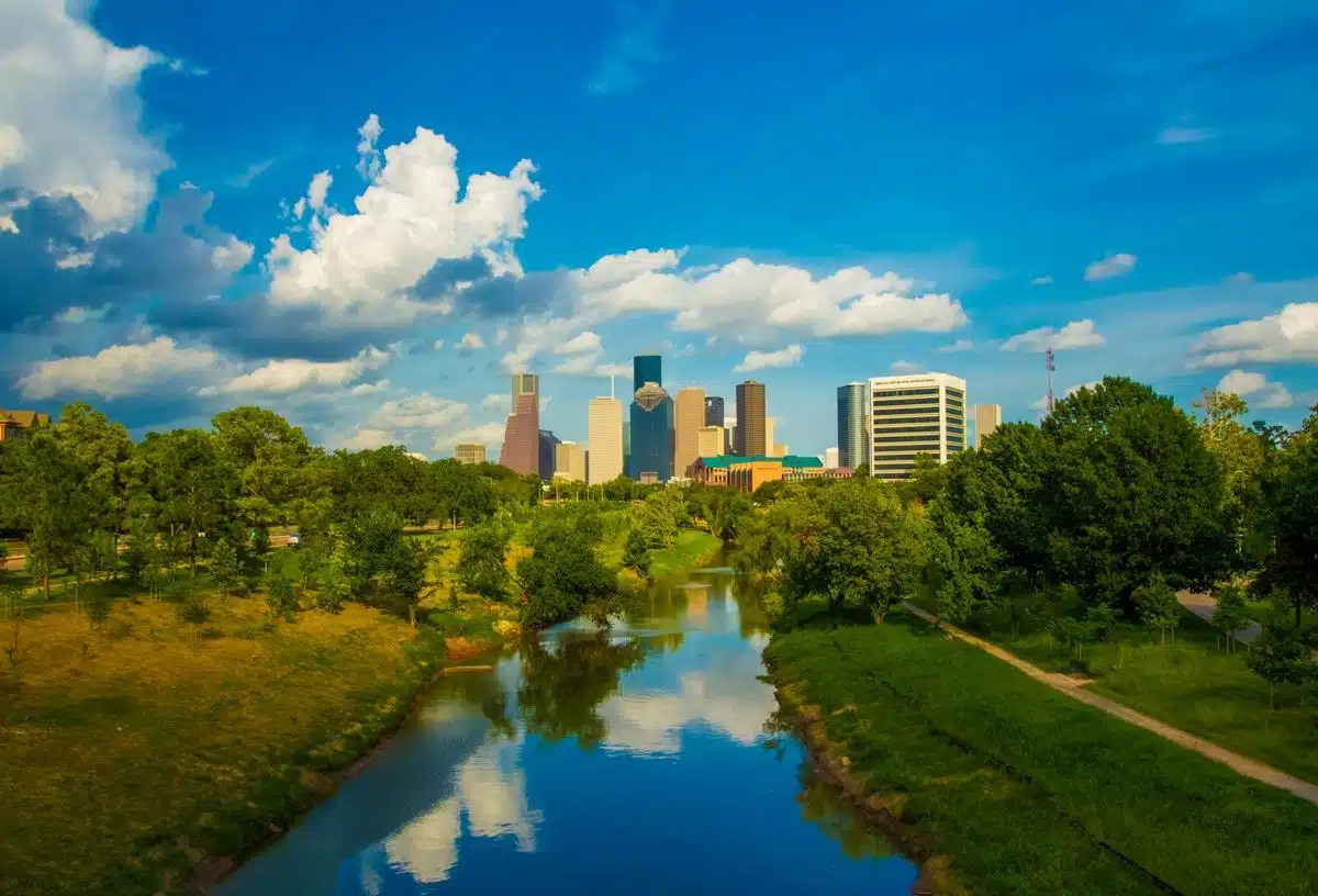 Houston, Texas skyline with a river and greenery under a bright blue sky.
