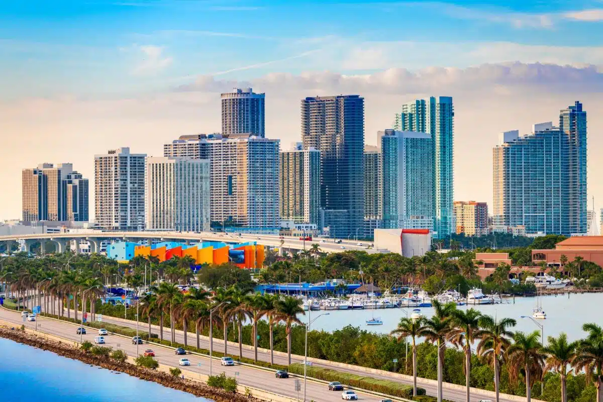 Scenic view of the Miami, Florida skyline with modern high-rise buildings, palm trees, and waterfront under a blue sky.