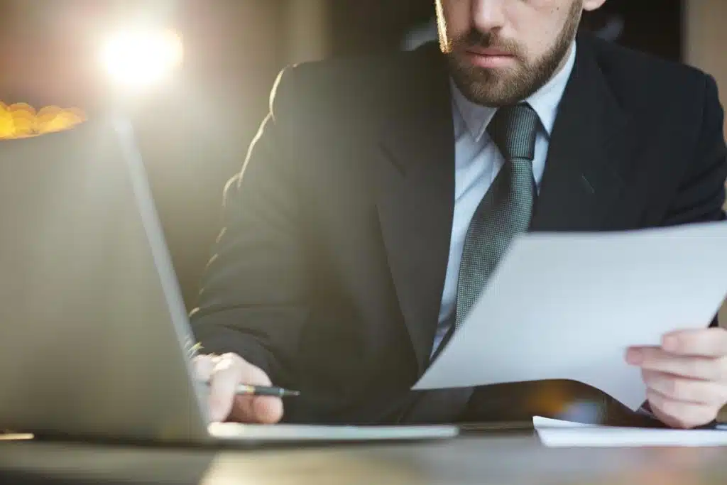 Tax lawyer in a suit analyzing IRS audit documents while working on a laptop in a softly lit office.