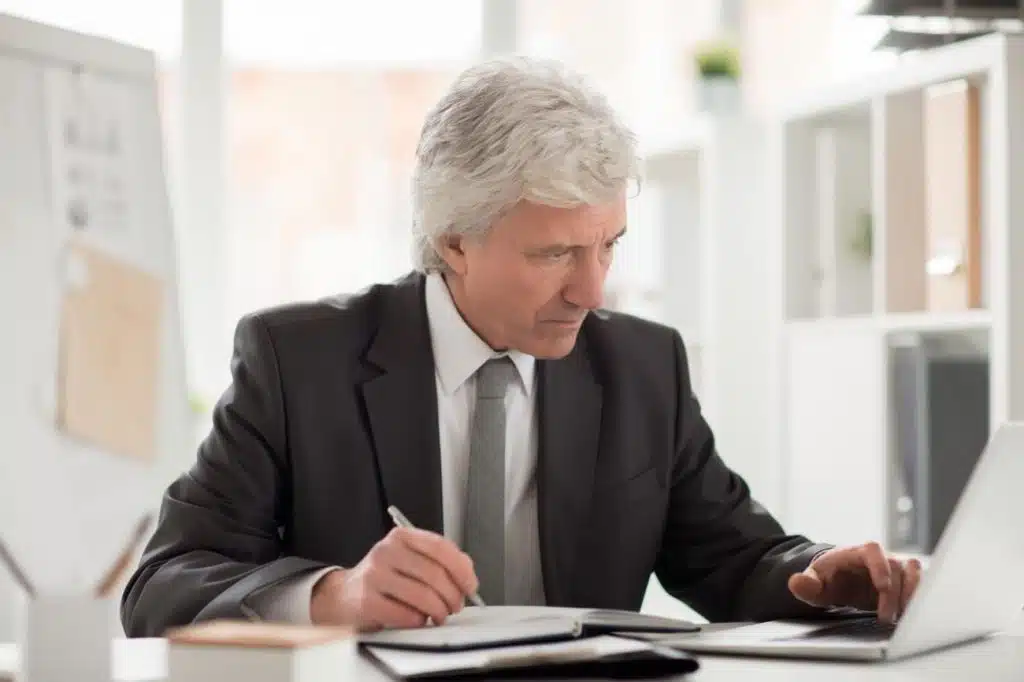 Seasoned unpaid taxes lawyer studies figures on a laptop and takes notes, illustrating focused expertise in settling overdue tax debts.