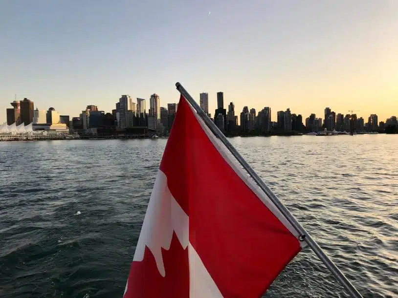 Canadian flag on a boat railing as it approaches a view of city buildings against a clear sky.