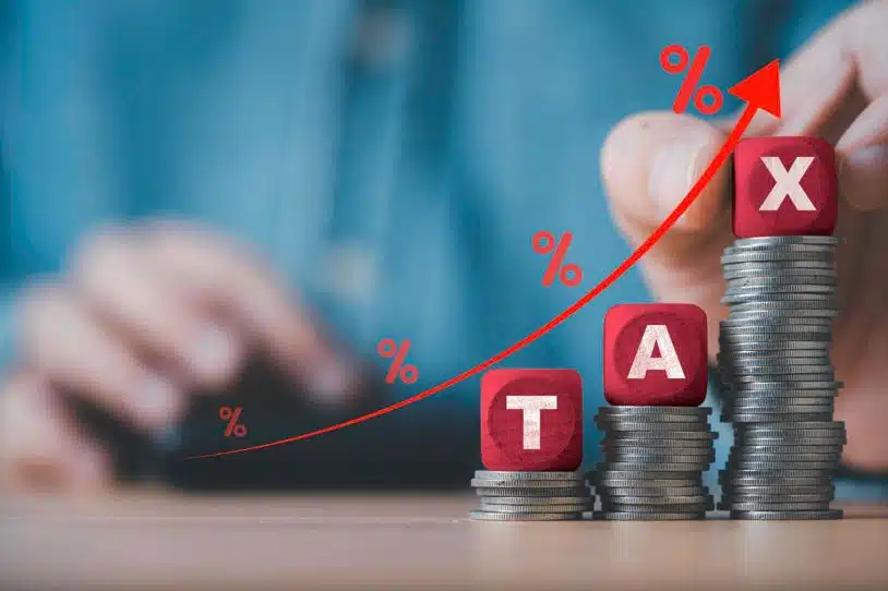 Three stacks of coins increasing in height topped with one wood block letter, spelling out the word the word Tax